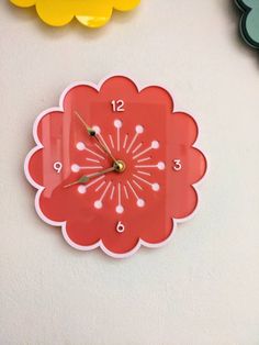 a red clock sitting on top of a white wall next to other colorful clocks and flowers