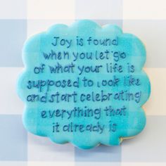 a cookie with a quote on it sitting on a checkered tablecloth background that says, joy is found when you let go of what your life is supposed to look like and start