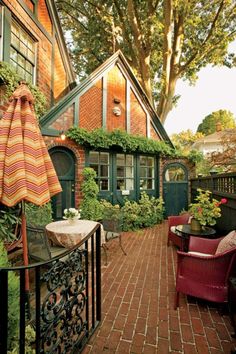 an outdoor patio with chairs and umbrellas next to a brick walkway in front of a house