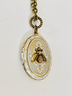 "This Bee locket featuring a brass oval vintage locket with lovely etching. I hand painted it in a shabby chic white. A tiny brass bee sits in the center. The locket hangs on a brass chain. You may choose your chain length at check out. The locket will arrive beautifully packaged and ready for gifting. Locket measures 1 and 3/8\" long and approximately 1 inch across." Vintage Charm Oval Locket Necklace, White Vintage Charm Medallion Jewelry, Vintage White Locket Necklace, White Vintage Medallion Jewelry With Charm, White Medallion Jewelry With Vintage Charm, Antique Oval White Necklace, Antique White Oval Necklace, Vintage Charm Oval Pendant Locket Necklace In Brass, Vintage Brass Locket Necklace With Oval Pendant