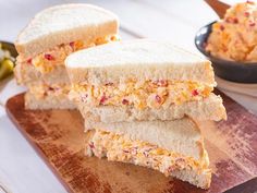 two sandwiches cut in half sitting on top of a cutting board next to a bowl of food