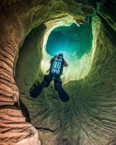 a man is in the middle of a cave with his back to the camera as he dives