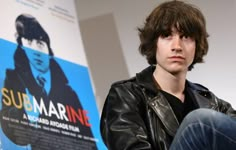 a young man sitting in front of a movie poster with his hand on his hip