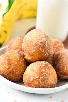 some sugared doughnuts are on a plate next to a glass of milk