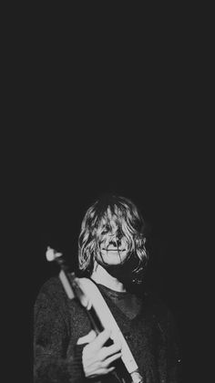 black and white photograph of a person holding a guitar in the dark with one hand