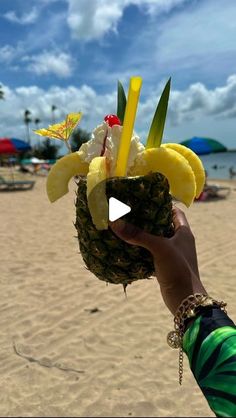 a person holding up a pineapple with bananas and other fruit on it at the beach