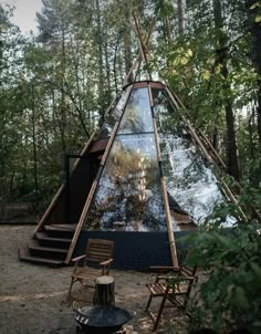 a teepee in the woods with chairs around it and stairs leading up to it