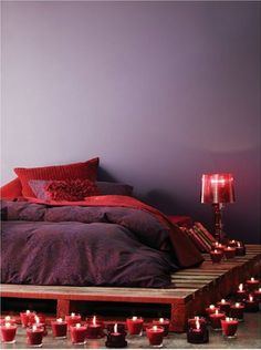 a bed with lots of red candles on the floor next to it and a purple wall in the background