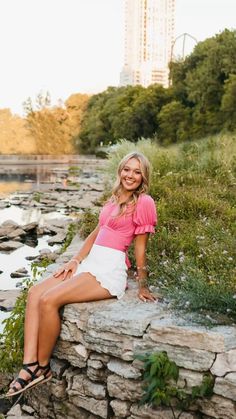 a beautiful woman sitting on top of a stone wall next to a body of water