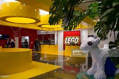 the inside of a lego store with yellow and red walls, large planters and sculptures