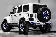 a white jeep with blue wheels parked in a garage next to a wall and door