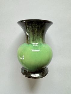 a green and black vase sitting on top of a white wall next to a hook