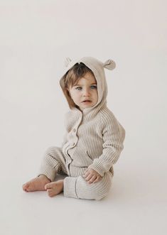 a little baby sitting on the floor wearing a sweater and pants with ears attached to it's head