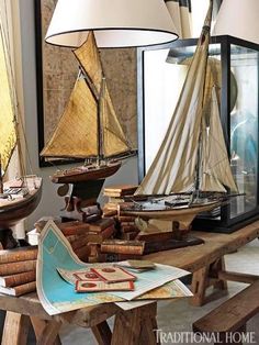 a table topped with lots of wooden boats next to a window filled with books and magazines