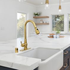 a white kitchen with marble counter tops and gold faucet sink, along with wooden cabinets