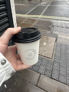 a person holding a coffee cup in their hand while standing on the sidewalk next to a building