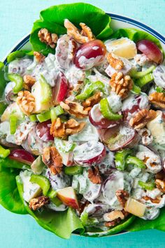 a salad with grapes, apples, walnuts and dressing in a bowl on a blue surface