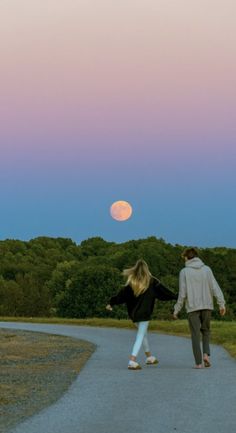 a man and woman walking down a path with the moon in the background