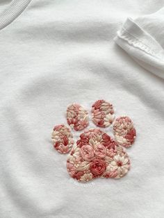 a white shirt with pink and red flowers on the front, embroidered onto it's chest