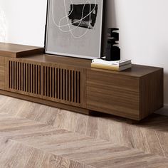 a wooden entertainment center with an art print on the wall above it and a book shelf below