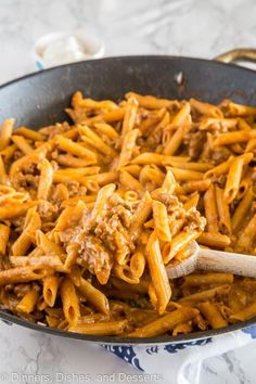 a skillet filled with pasta and meat in sauce on top of a marble counter