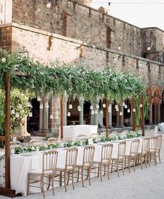 an outdoor dining area with tables and chairs covered in greenery, surrounded by stone buildings