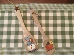 two wooden spoons with designs on them sitting on a checkered cloth tablecloth