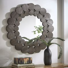 a round mirror sitting on top of a wooden table next to a vase and book