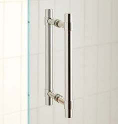 a close up of a metal handle on a glass shower door with white tiles in the background