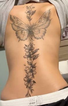 the back of a woman's stomach with flowers and a butterfly tattoo on it