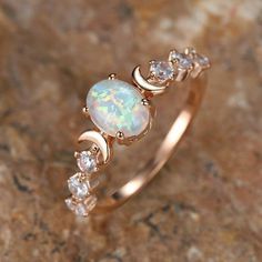 a white opal and diamond ring sitting on top of a rock