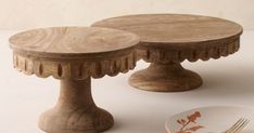 two wooden cake stands sitting next to each other on a white tableclothed surface