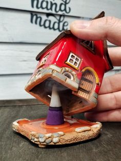 a hand holding a small red house on top of a wooden table