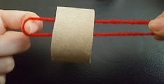 a person is holding a roll of toilet paper and stringing it with red yarn