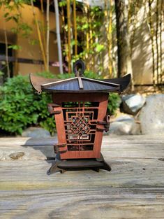 a small wooden lantern sitting on top of a wooden table next to some rocks and trees