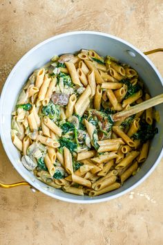 pasta with spinach and mushrooms in a pan on the counter top next to a wooden spoon