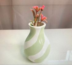 a green and white vase with pink flowers in it on a counter top next to a wall