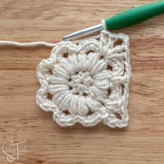 the crochet square is being worked on with a green handled knitting needle in front of it