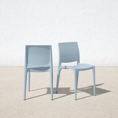 two blue chairs sitting next to each other in front of a white wall and cement floor