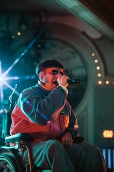 a man in a wheel chair singing into a microphone while holding a microphone up to his mouth