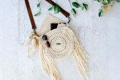 a white purse with tassels on top of it and some leaves around it