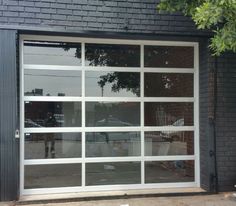 an open garage door on the side of a black brick building with trees in front of it