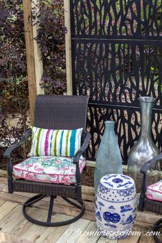 two chairs sitting on a wooden deck with vases next to them and an iron screen in the background