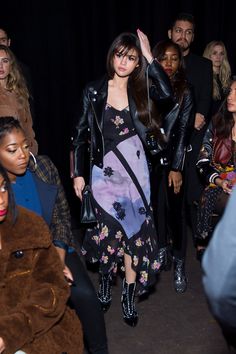 a group of people standing around each other in front of a black curtain and one woman is wearing a floral dress