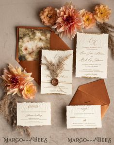 the wedding stationery is laid out with flowers and feathers on it, along with two matching envelopes