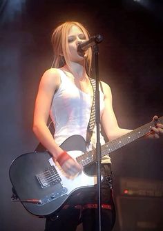 a woman holding a guitar while standing in front of a microphone