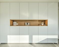 an empty room with white cupboards and wooden shelves on the wall next to it