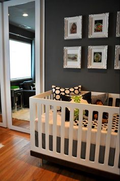 a white crib in front of a black wall with pictures on it and a wooden floor