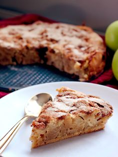 a white plate topped with a slice of cake next to green apples and a fork