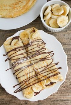 pancakes with chocolate drizzled on them and bananas in bowls next to it